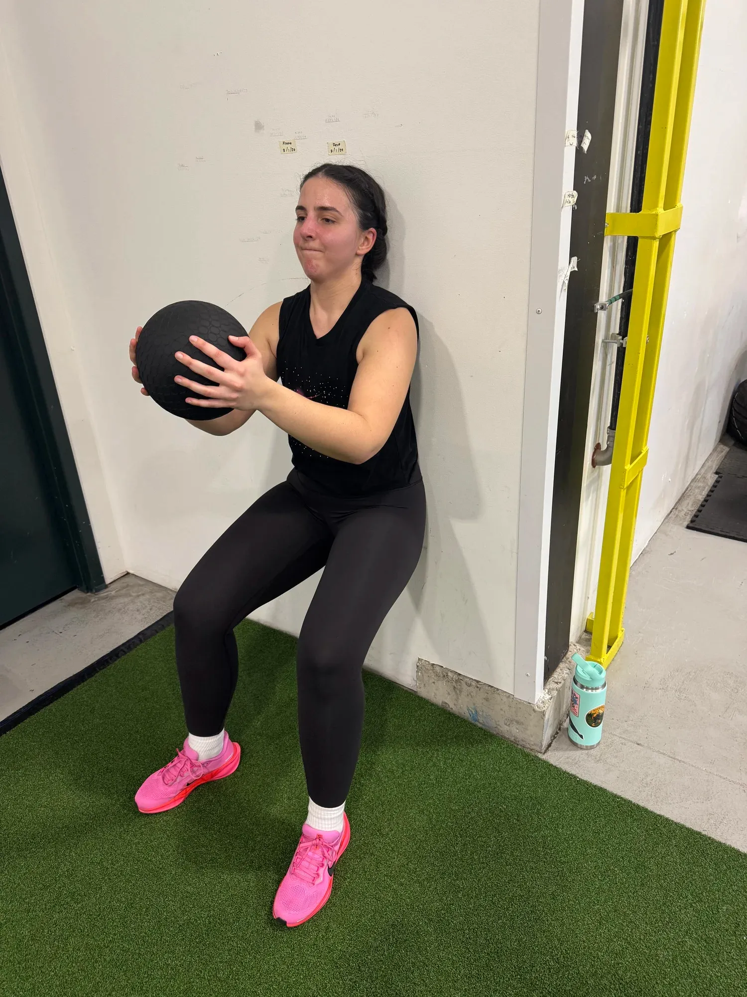 A student holding a wall sit with a medicine ball during a group class